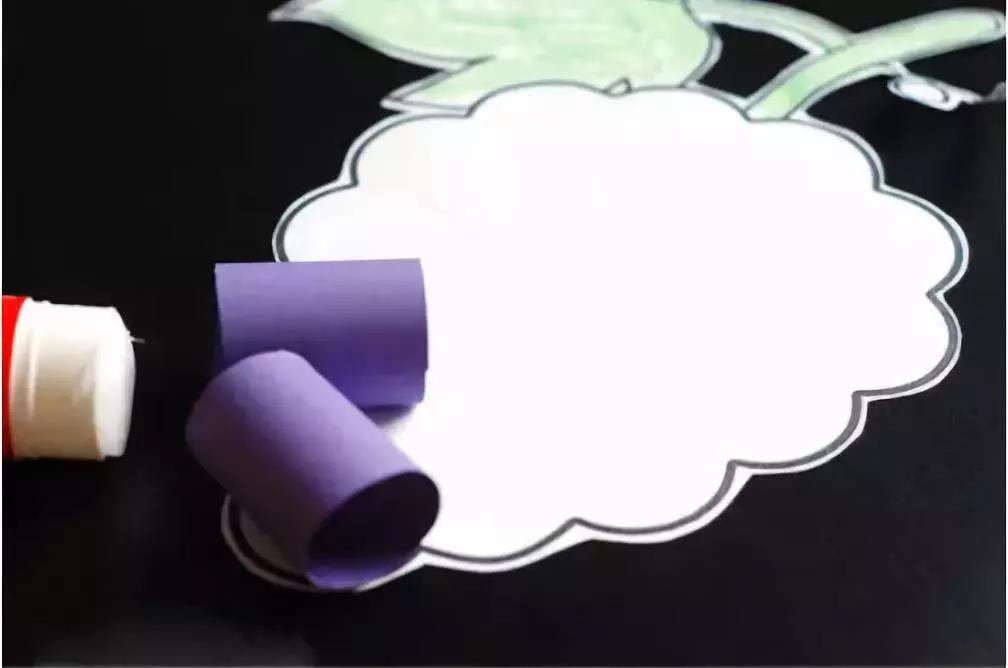 步骤2：紫色卡纸对折，并如图剪取，紫色的长条绕手指，使其卷曲。并将葡萄模板剪下来。