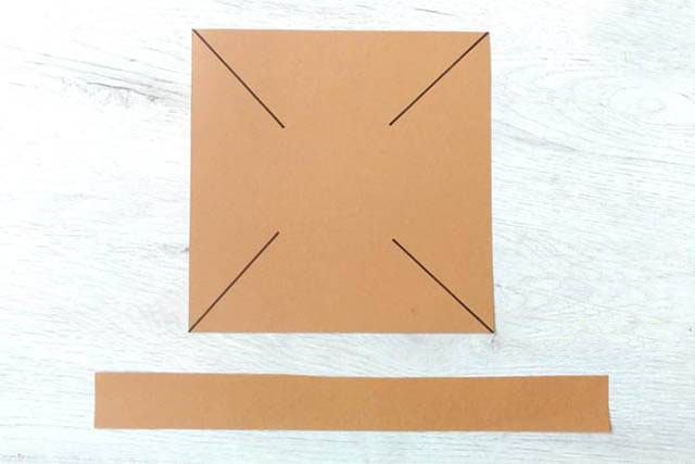 步骤2：取1张15厘米边长的正方形卡纸，从每条对角线的两端分别向内剪开5-6厘米长。另外剪1条2.5x25厘米长的矩形纸条作为篮子的提手。（用你手头方便的工具来装饰正方形和矩形提手，不管是蜡笔或者贴纸都可以。）