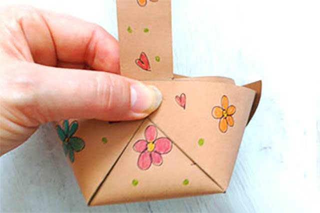 步骤6：捏住重叠在一起的角，将提手的一端放在这些角的内侧，用订书机将它们固定在一起。