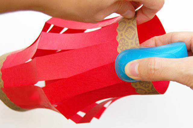 步骤12：装饰之后，将纸张的两条窄边圈在一起，把纸张变成圆筒状。窄边互相重叠大概1.5厘米左右，用胶水或者订书机固定在一起，灯笼的主体就做好了。