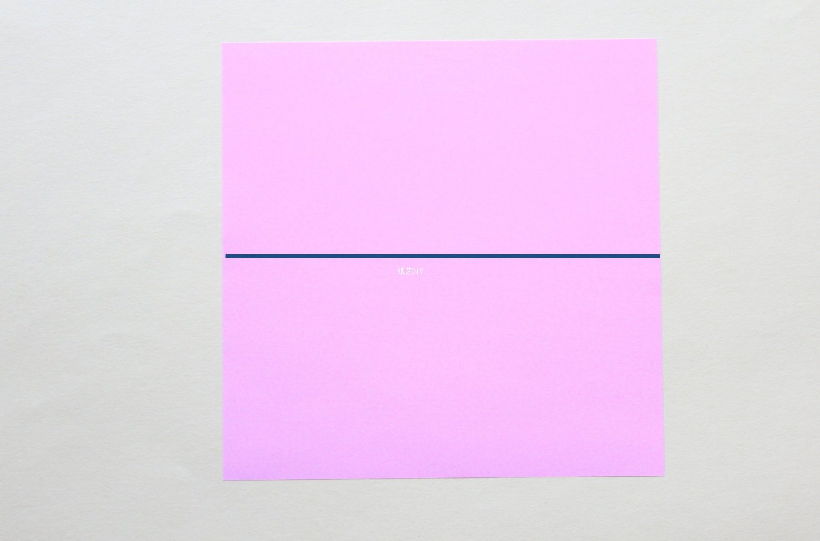 步骤1：首先，宝宝们准备一张自己喜欢的彩色折纸，沿着图中的实线位置对半进行折叠，折出相应的折痕后，并展开。