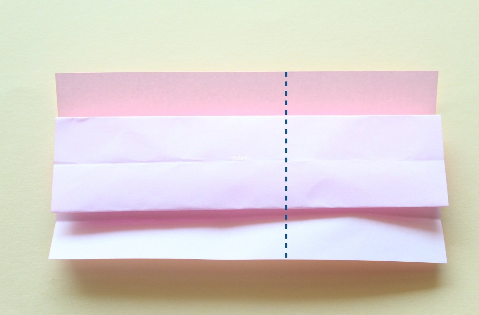 步骤4：将折纸下侧沿着折痕叠加一层，沿着图中的虚线位置向其右侧翻折。