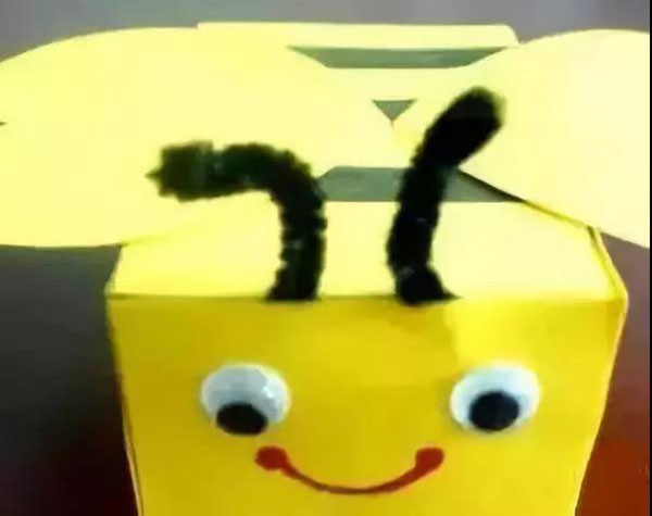 步骤6：用两个扭扭棒当做蜜蜂的触角，装饰在牛奶盒上，然后给蜜蜂装上眼睛，用红色笔画上嘴巴.