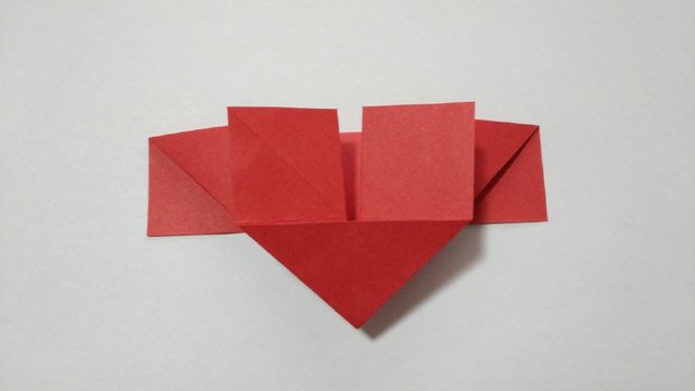 步骤5：然后，这里把刚才对折好的左右2边的纸张，沿着折痕往中间对折，然后把中间压下去，折平，折出一个小三角，就是下图的样子。