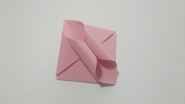 步骤6：然后翻到纸张的反面，把纸张先从中间往前对折一下，然后用小木棍把2个三角卷起来，卷出下图的样子。这样折纸花球的一个部件就折好啦。