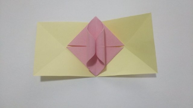 步骤8：然后把折纸花球的粉色部件放在黄色纸张折好的折痕中间，注意对齐位置。