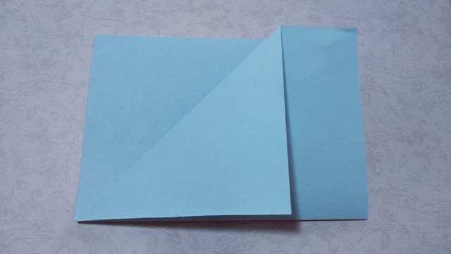 步骤2：然后开始来做，先把A4纸左右对折，然后把前面纸张的顶端往下对折，对折出三角形状来。