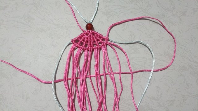 步骤17：接着再在右端每打一个斜卷结再加一条30cm的粉线挂雀头结，2边是对称的。这一排一共挂了6个雀头结。
