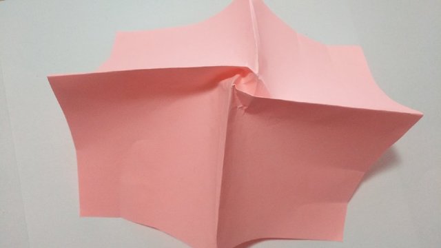 步骤5：折痕对折出来之后，翻到正面，用2只手抓住这4条边往里挤，一边挤一边旋转，中间的小正方形往下压，就会折出来玫瑰花芯。