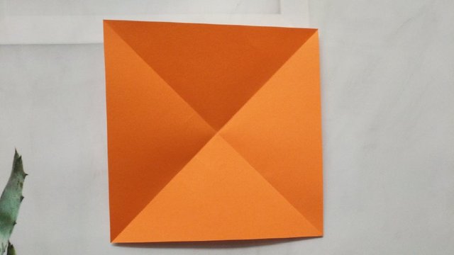 步骤7：饺子盘折好了，现在我们来做折纸饺子，取一张彩色的正方形纸，纸张不要太大，我这里10cm左右，然后把正方形纸斜向交叉对折，折出折痕。