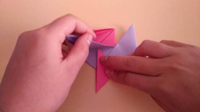 步骤14：压下去之后把玫红色纸底下的小角往上对折，角塞到紫色的纸张底下