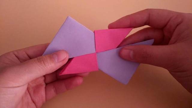 步骤16：接着上面的玫红色的纸张的角也是同样的往下对折，然后把角塞到紫色的纸底下藏起来