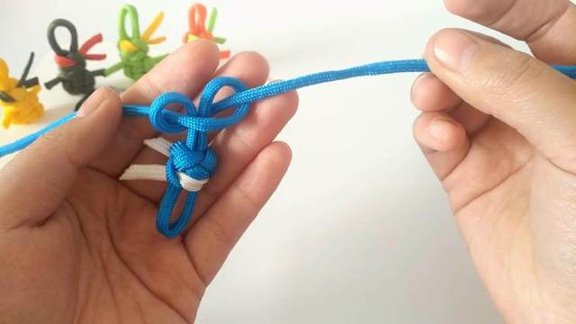 步骤19：右边绳子从左边绳子底下绕一个圈穿到左边的孔里，然后拉紧