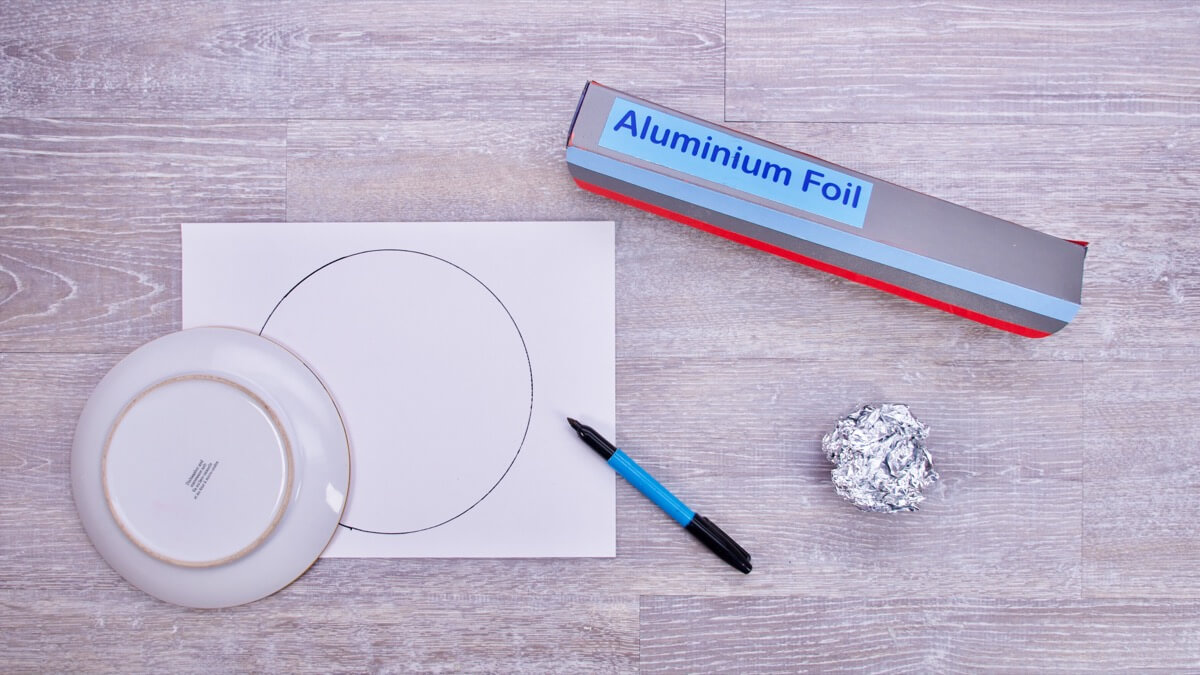 步骤1：弄碎一块铝箔纸，捏成一个小球。把小球底部放在平台上轻轻地弄平，并形成一个小手柄。用记号笔在白色卡纸上借助你的工具画圆。