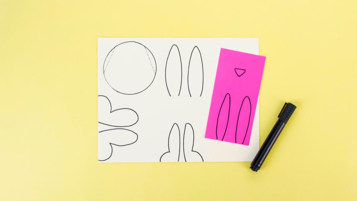 步骤3：将纸杯的顶部放在一张卡纸上。然后在圆的两边画两条线，做成兔子的头。画一些长耳朵，两只前爪和两只脚用脚。在粉红色的卡纸上画兔子耳朵的内部和小鼻子。剪出所有形状。