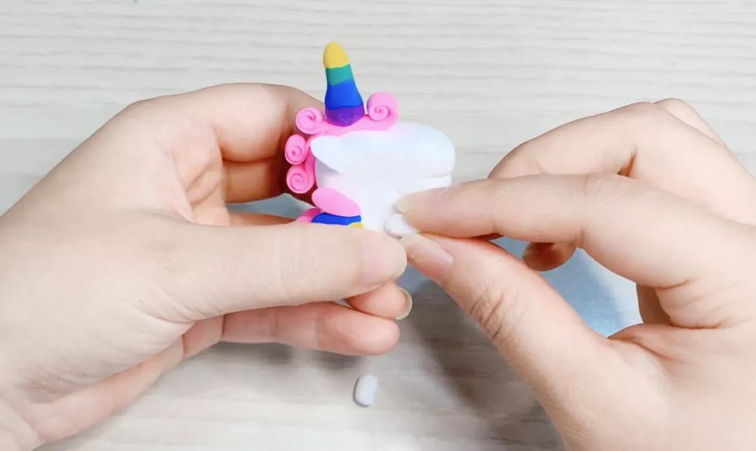 步骤13：将两块白色黏土捏成圆柱，做成独角兽的前肢，粘在头下方。