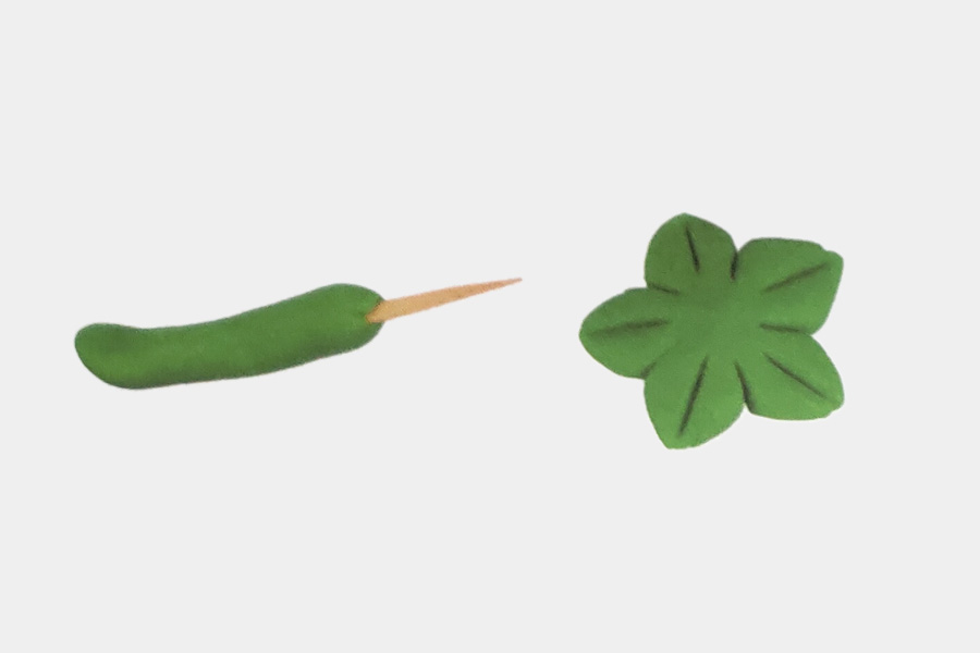 步骤3：在长条上插根牙签作为茎，用扁圆捏出花形辣椒根蒂。