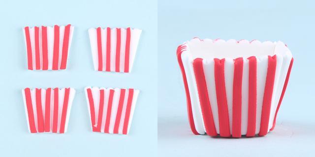 步骤2：红色粘土剪成细条一条条竖着粘在白色梯形片上，顶部剪出锯齿状，把薄片粘到做好的梯形体上，这样爆米花盒子就做好了。