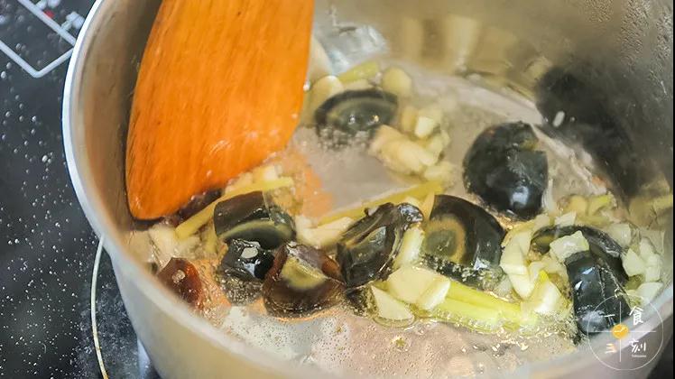 往锅中倒油，油热后放入蒜粒、姜丝煸炒至微微金黄，倒入皮蛋翻炒几下