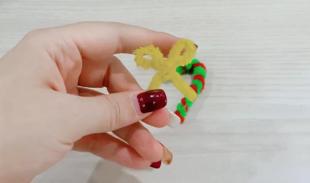 步骤4：选一根黄色的扭扭棒，一头绕一个圈后扭转再将另一头绕一个圈，剪去多余的部分。