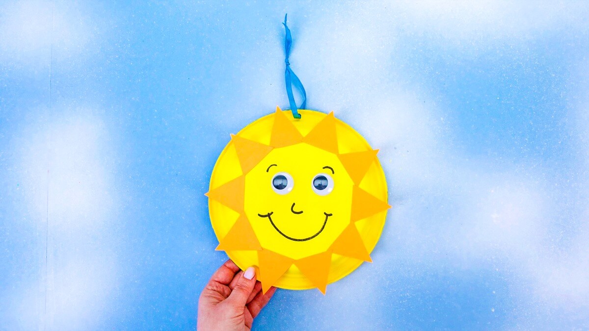 步骤11：在盘子的顶部中心打一个孔。将色带穿过孔，并在末端打一个结。画太阳的脸，然后粘上眼睛，并将悬挂点置于中央顶部。