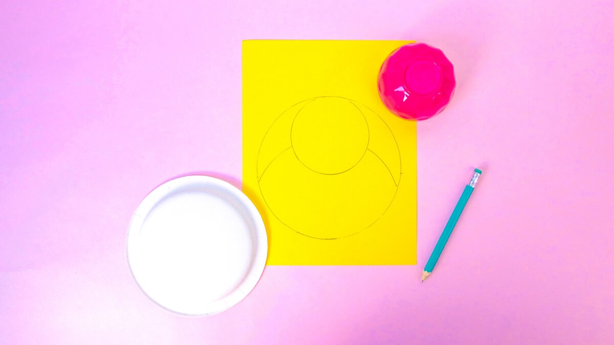 步骤2：首先，将纸碟的圆形描在黄色的纸上。要使头部成形，请使用较小的碗，并将其描绘纸盘圆的上边缘内，在圆内形成一个圆。再用一次纸板从小圆圈向外延伸到大圆圈边缘的线，大约在小圆圈的一半处。剪出小鸡的形状。