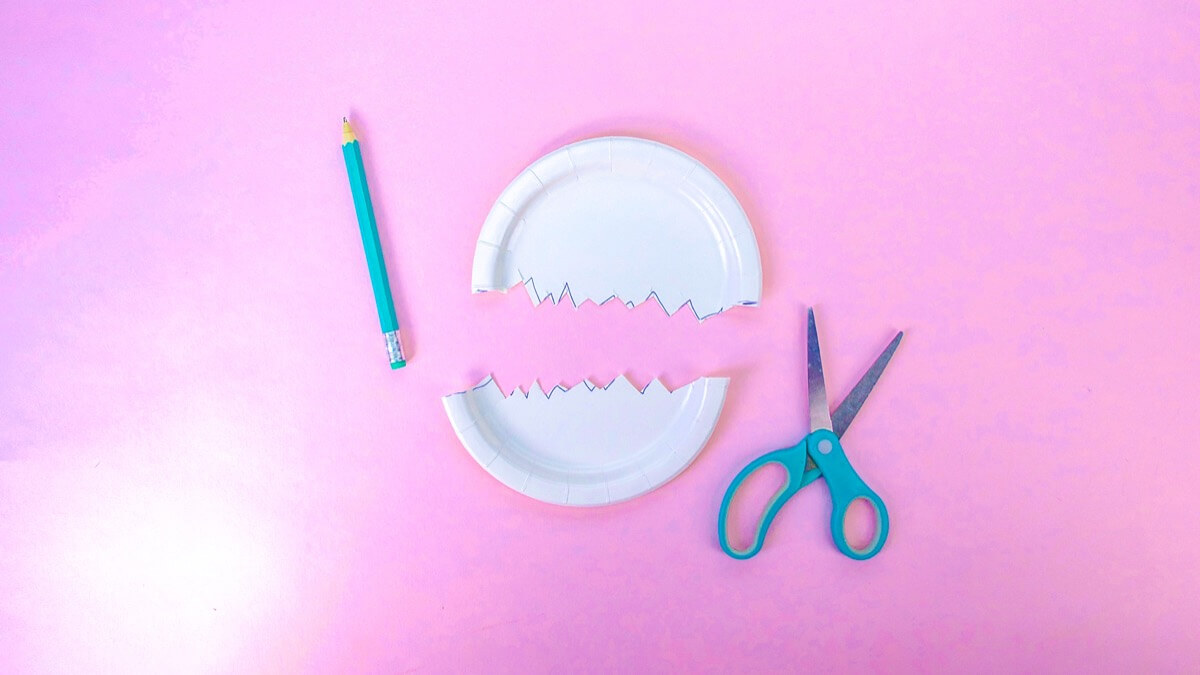 步骤4：开始做鸡蛋了。在纸盘的中心画一条裂纹线，然后沿着锯齿形将其剪成两半。