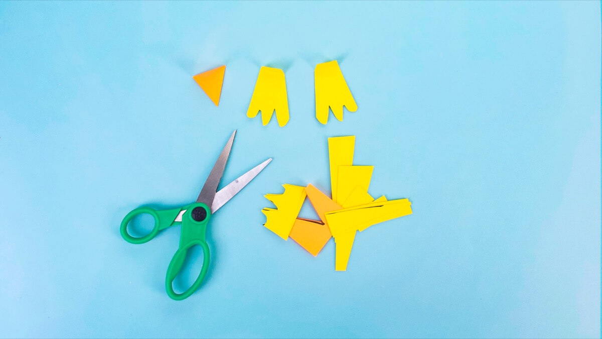 步骤6：要使企鹅的嘴，将一小块橙色的建筑纸对折，然后从折叠的一面切成三角形。对于蹼状脚，将两张工作纸叠放在另一只脚上，然后切成三角形，每只脚上三个脚趾。 