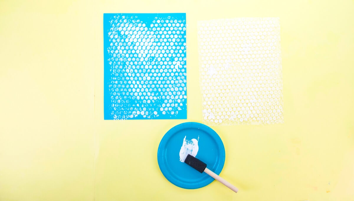 步骤2：首先在气泡包装纸上涂一层白色涂料。有些孩子可能更喜欢用手指，而另一些孩子会喜欢使用画笔或海绵刷。将气泡包装纸放在蓝色卡片纸的顶部，然后向下压以转移涂料。慢慢撕下蓝纸，放在一边晾干。