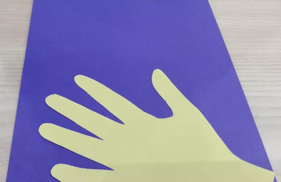 步骤2：贴在深色卡纸底部，注意大拇指的位置不要贴反了哦~你也可以先不固定，待花花贴好后再固定。