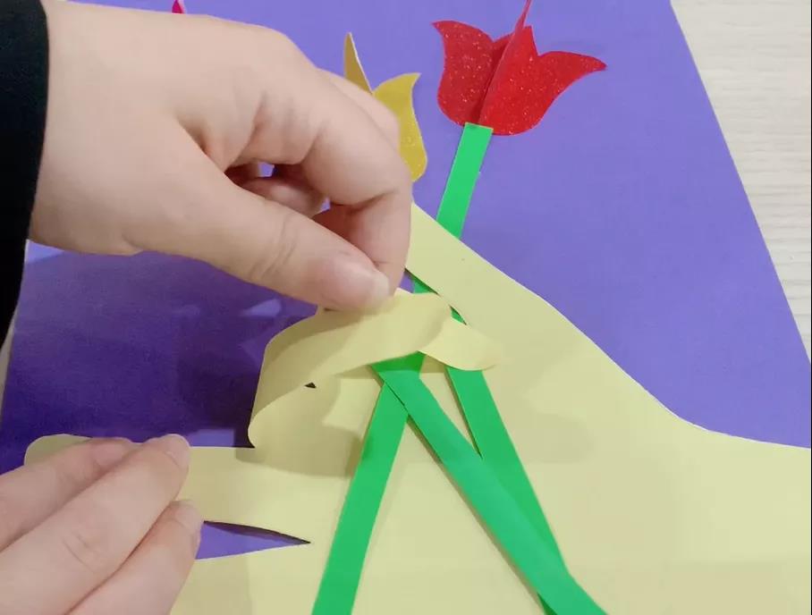 步骤7：给每个手指贴上双面胶往手心贴去，仿佛是手握住花束的样子，此时可以把整个手固定贴在深色卡纸上。送给妈妈的创意画就做好啦！