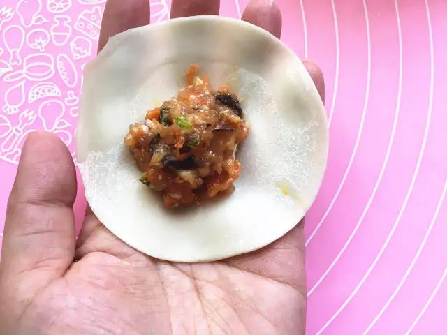 取一张饺子皮，将适量馅料放置饺子皮中间，四周抹少许水。