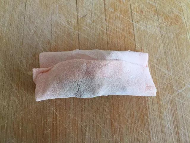 取适量的饺子馅放到正方形饺子皮中间，下边向中间折叠，边缘抹少量水，上边也折回来与抹水部分重叠粘好。