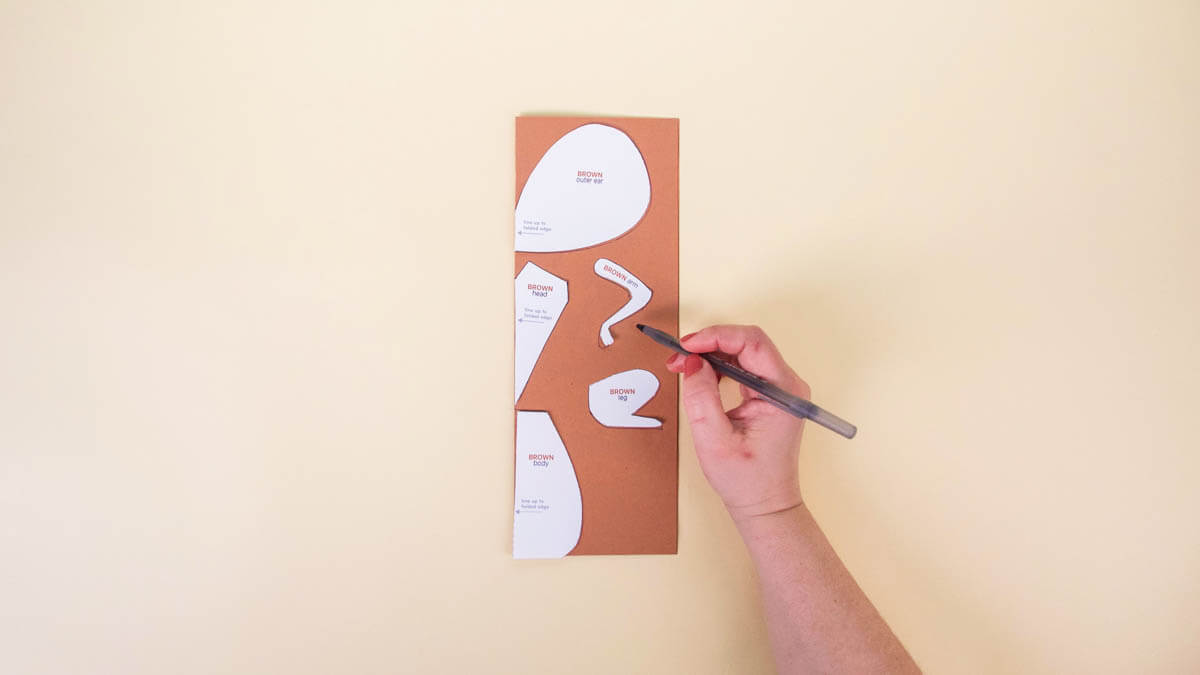 步骤5：将棕色的建筑纸横向对折。将头部、腹部和耳朵模板与纸的折叠边缘对齐。