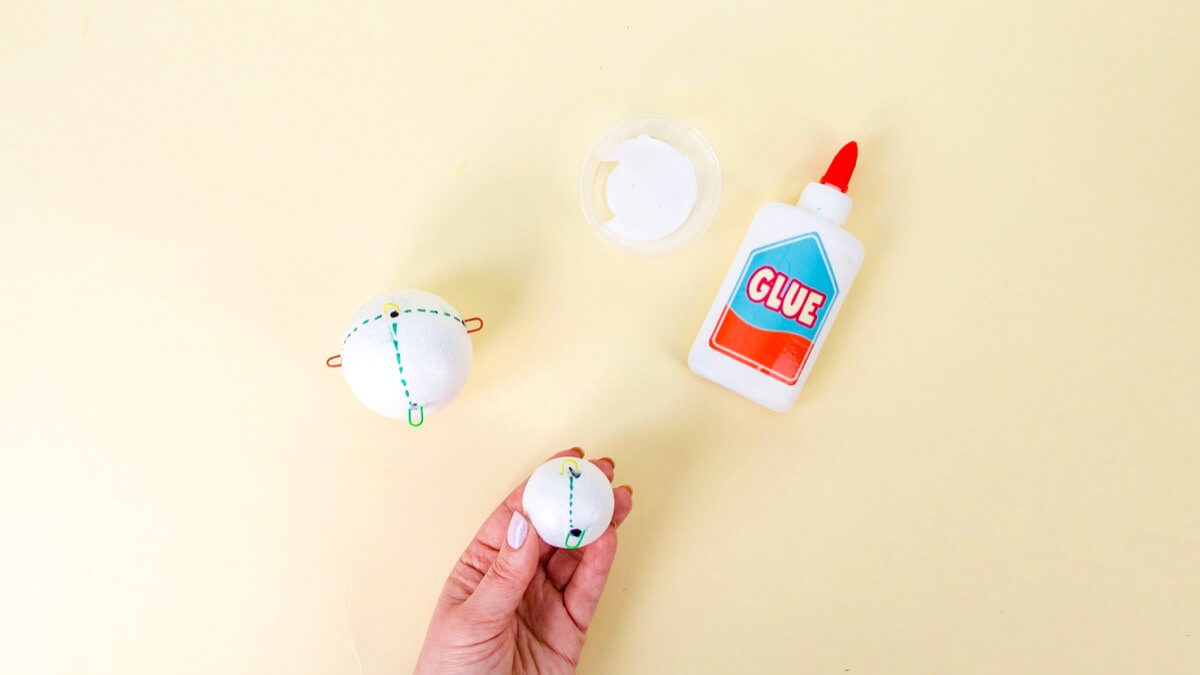 步骤4：将回形针的一半浸入白胶中，然后将它们刺入泡沫球中。