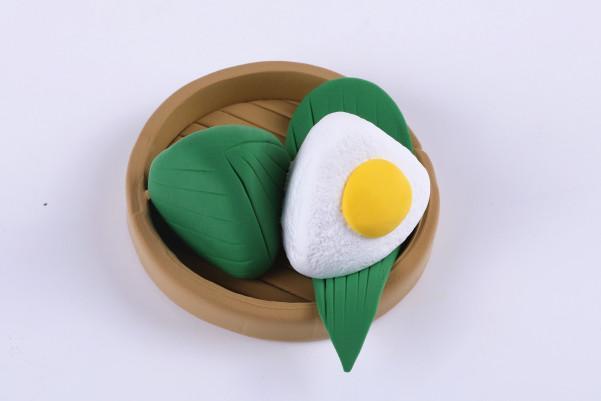 步骤6：用白色粘土做出三角的糯米粽子，用黄色粘土做一个圆形蛋黄粘在上面，如图所示。