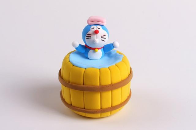 步骤7：把做好的哆啦A梦放到大木桶里，安上两只胳膊并做好造型。用粉红色粘土做一块折叠的毛巾放在哆啦A梦的头顶。