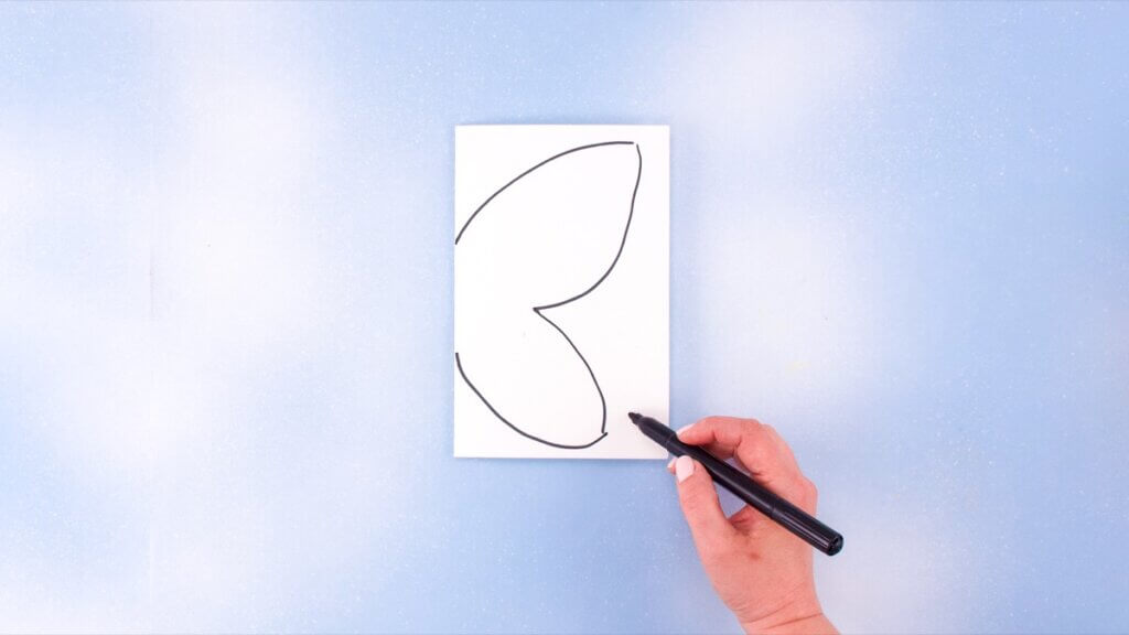 步骤2：首先将你的白纸对折。在折叠纸的一侧，画出蝴蝶翅膀形状的一半。