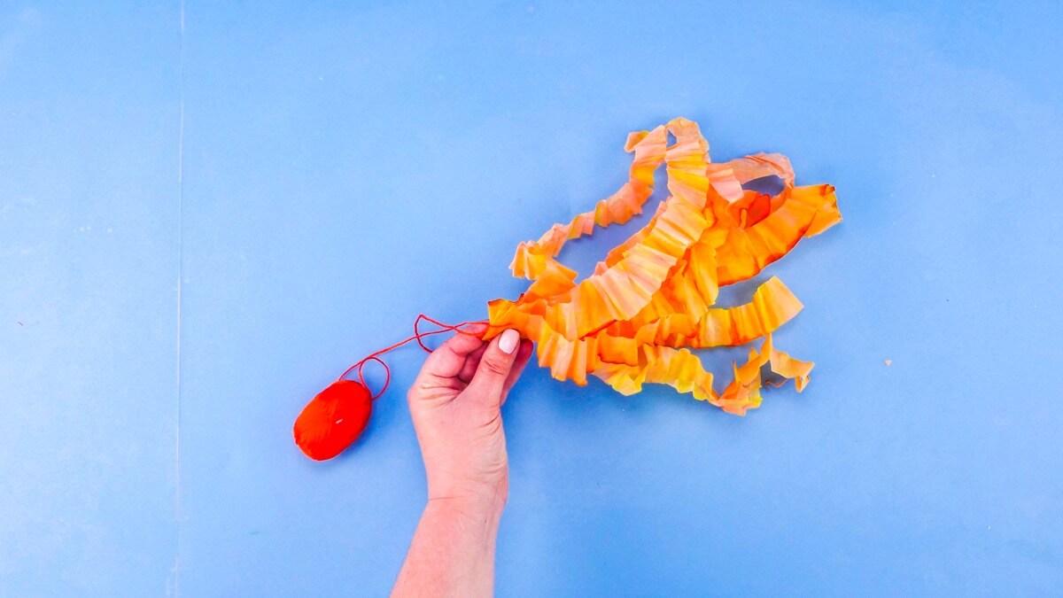 步骤10：将这些条带对折，使两端的长度错开。将所有折叠的末端聚集在一起。握住所有的褶皱，再次折叠它们并用剪刀剪一个小孔（或用打孔器打一个孔。）