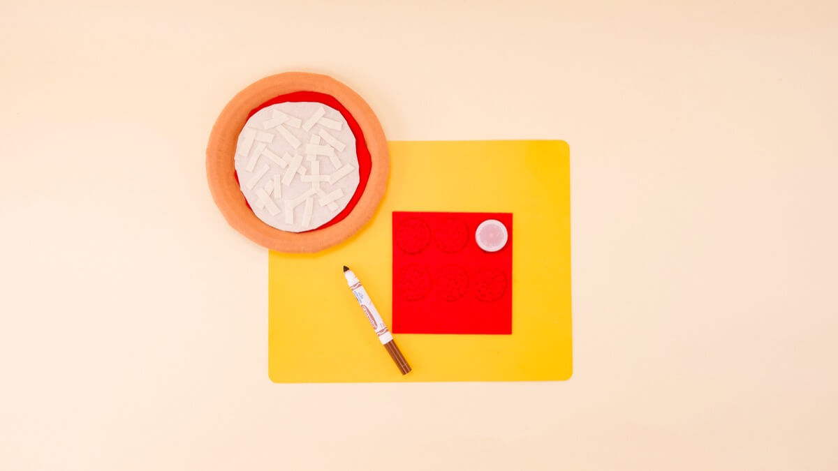 步骤8：制作意大利辣香肠，在一块红色毛毡上画出瓶盖（或圆形的东西）。把它们剪下来，用棕色记号笔画一些小点，这样它们看起来更像意大利辣香肠。 