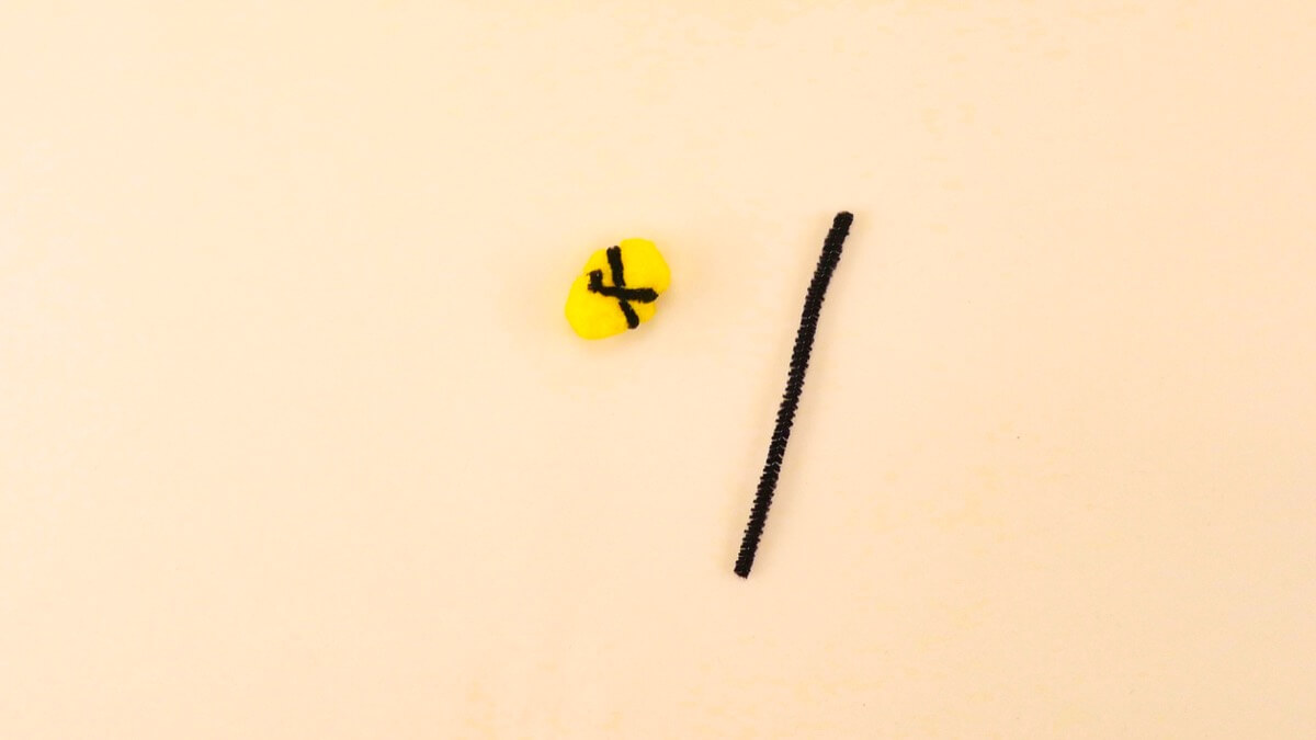 步骤7：首先将黑色扭扭棒切成两半。然后将它们包裹在黄色绒球上。将它们包裹起来时，最容易在一侧形成 X 形。