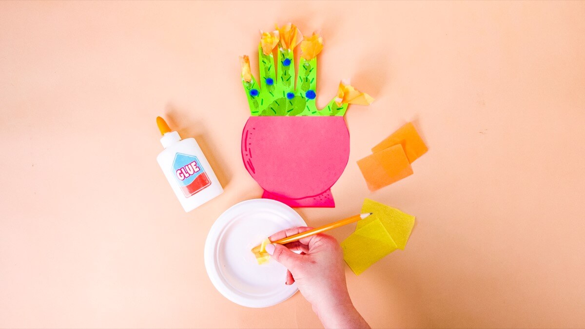 步骤7：我们添加了一些彩色绒球和纸巾方块来制作花朵。我们将纸巾方块包裹在铅笔的橡皮擦末端，然后将其浸入一些白胶中