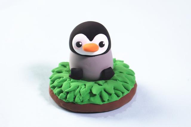 步骤8：把企鹅放到草地上，然后用黑色粘土揉两个圆球做企鹅的双脚。