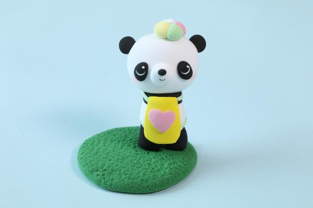 步骤9：用黄色粘土做一个小围裙给熊猫围上，上面装饰上粉红色的小心心。