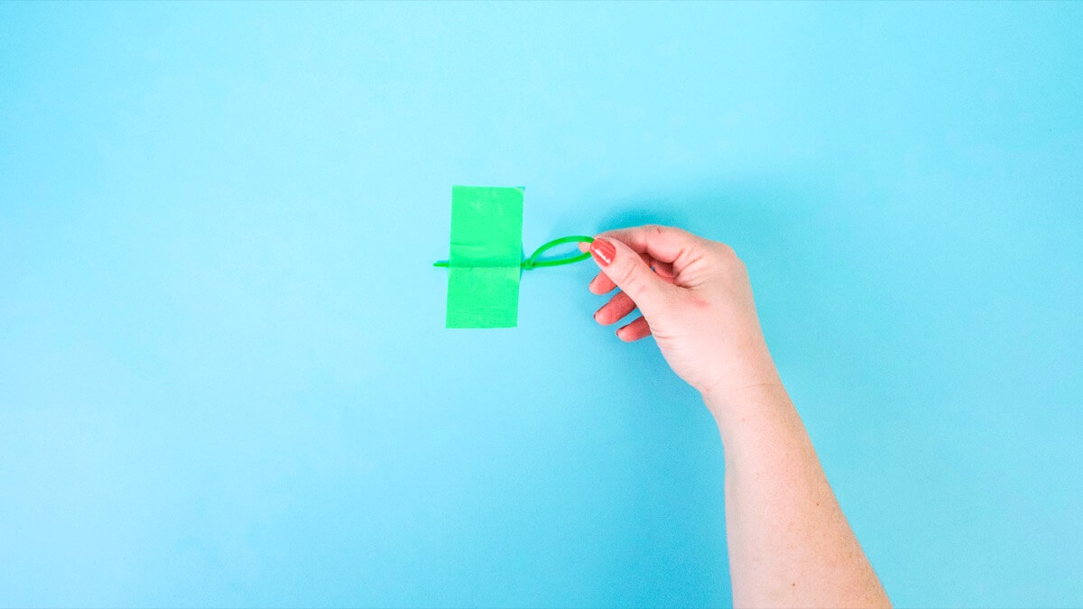 步骤6：现在我们将使用一个称为 Lark 结的简单结将丝带连接到拉链环上。首先将每段缎带对折，然后将其折回自身。然后，一次一根丝带，将丝带的两端穿过扎带的环，然后穿过丝带的折叠端。拉动丝带的末端以固定结。 