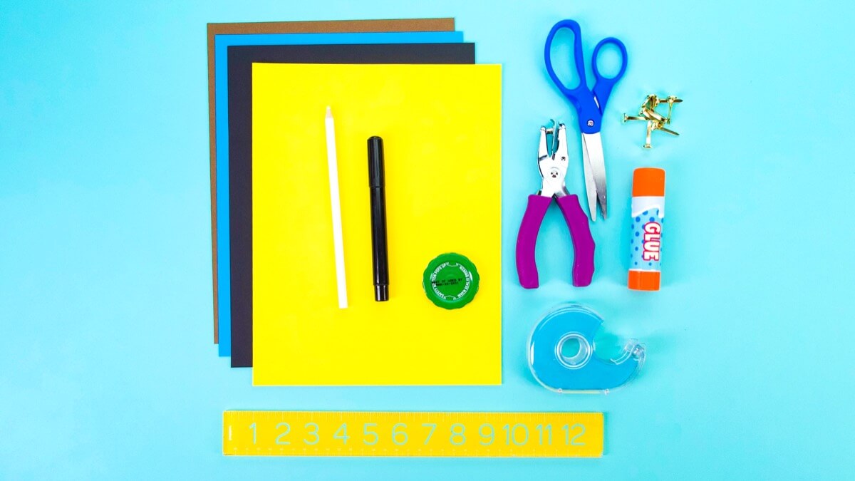 步骤1：材料准备几种不同颜色的建筑纸。我们使用了黄色、黑色和蓝色。磁带、记号笔、胶棒、圆头紧固件、打孔机、尺子、瓶盖或圆形的东西可以追踪以制作轮子。白色铅笔蜡笔 - 在黑纸上描画