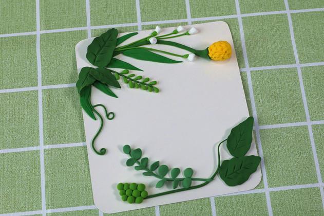 步骤6：用白色粘土做一些小花苞，绿色粘土做一些椭圆形的小叶子做好造型粘在上面，这样绿叶的背景就做好了。