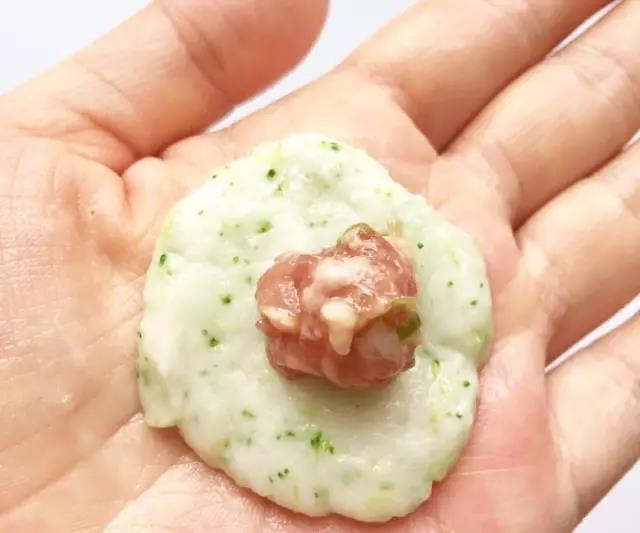 手沾上水取一小块鱼泥压扁，中间抠一个小洞放入少许肉糜，食指沿着鱼泥的边缘向上推收口，揉成圆圆的鱼丸。