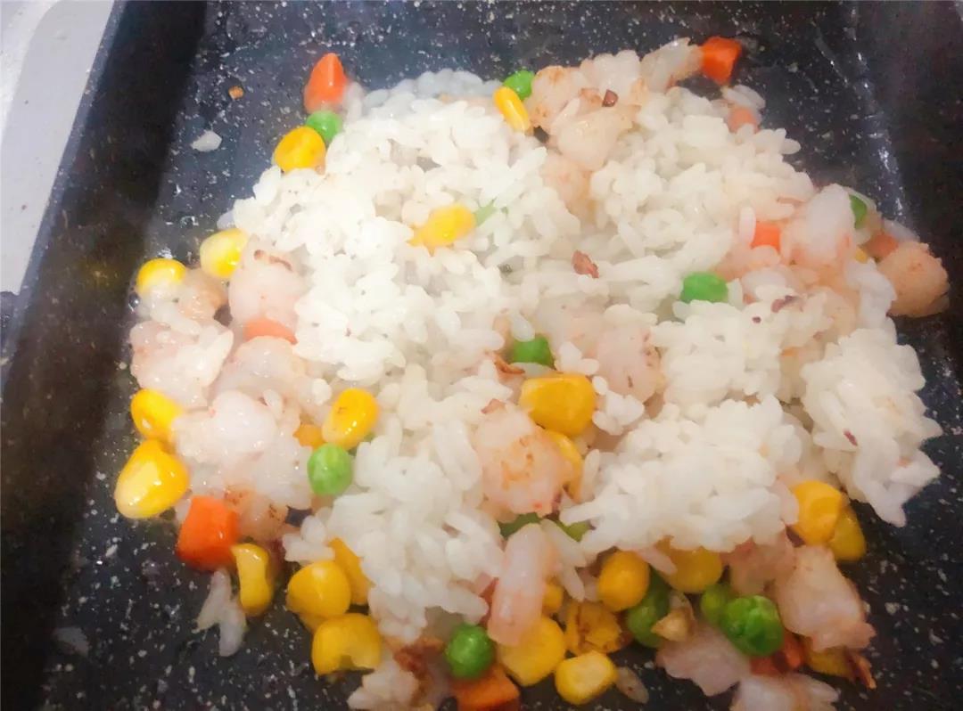 待虾仁变色后倒入米饭翻炒均匀，加入少许开水，焖煮片刻。