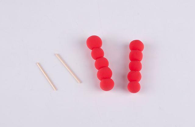步骤4：下面我们开始做糖葫芦啦！把牙签两头的尖尖剪掉，只留中间一段，做糖葫芦的签子。然后用红色粘土揉若干个小圆球，然后把他们插在签子上面，如图所示，就是糖葫芦串了。
